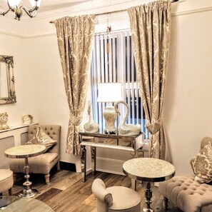 A room with a classic design, featuring a tufted armchair, a small round table, a vintage-style lamp, and a decorative vase on a console table. - Serendipity House (Londonderry)