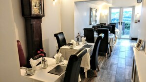 A dining area with tables set for service, a large wall clock, and a view through the door. - Serendipity House (Londonderry)