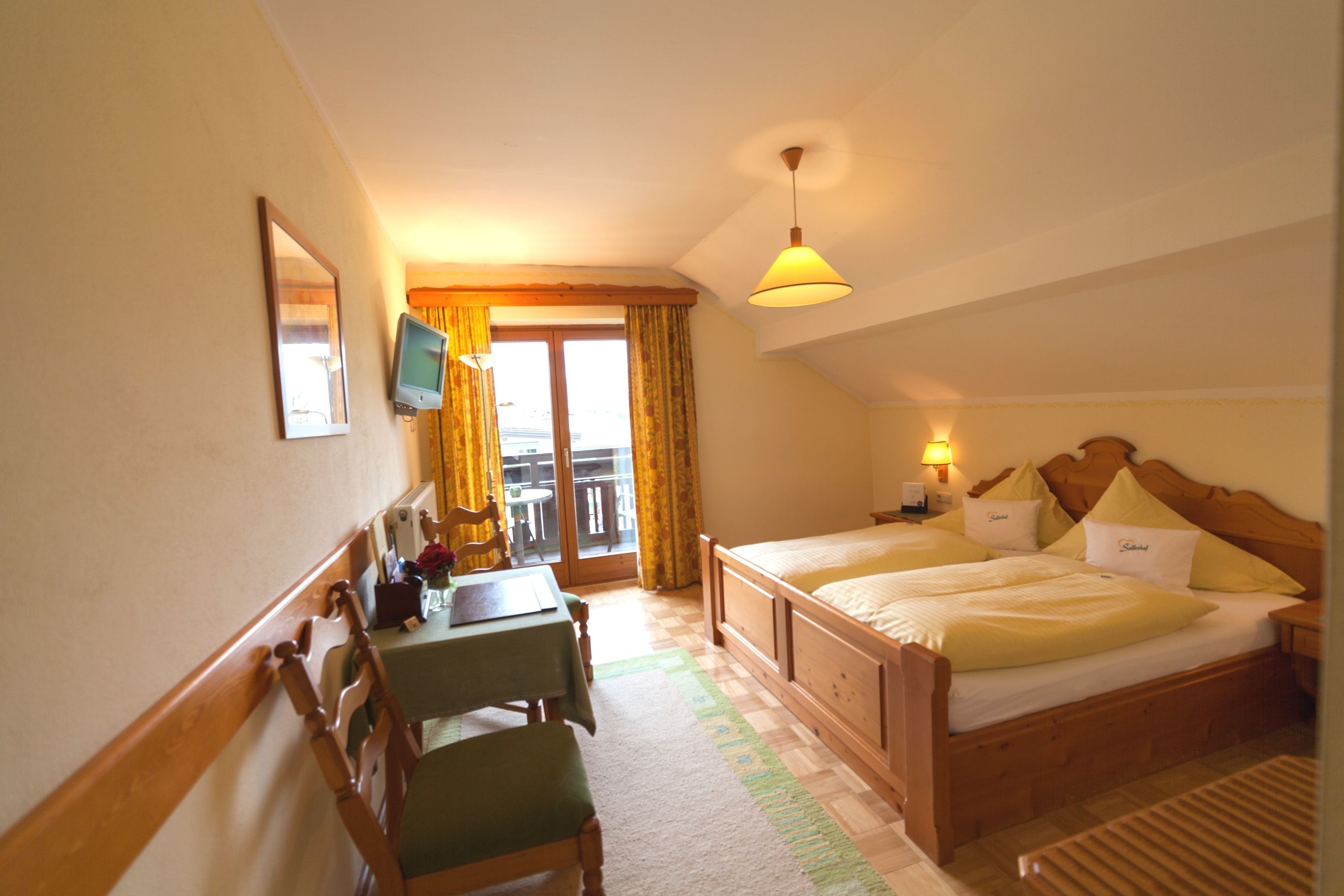 A hotel room with a bed, a desk with a chair, a television, and a balcony with curtains.
