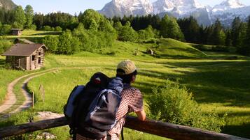 A person leaning on a wooden fence overlooking a mountainous landscape with a small cabin in the foreground.