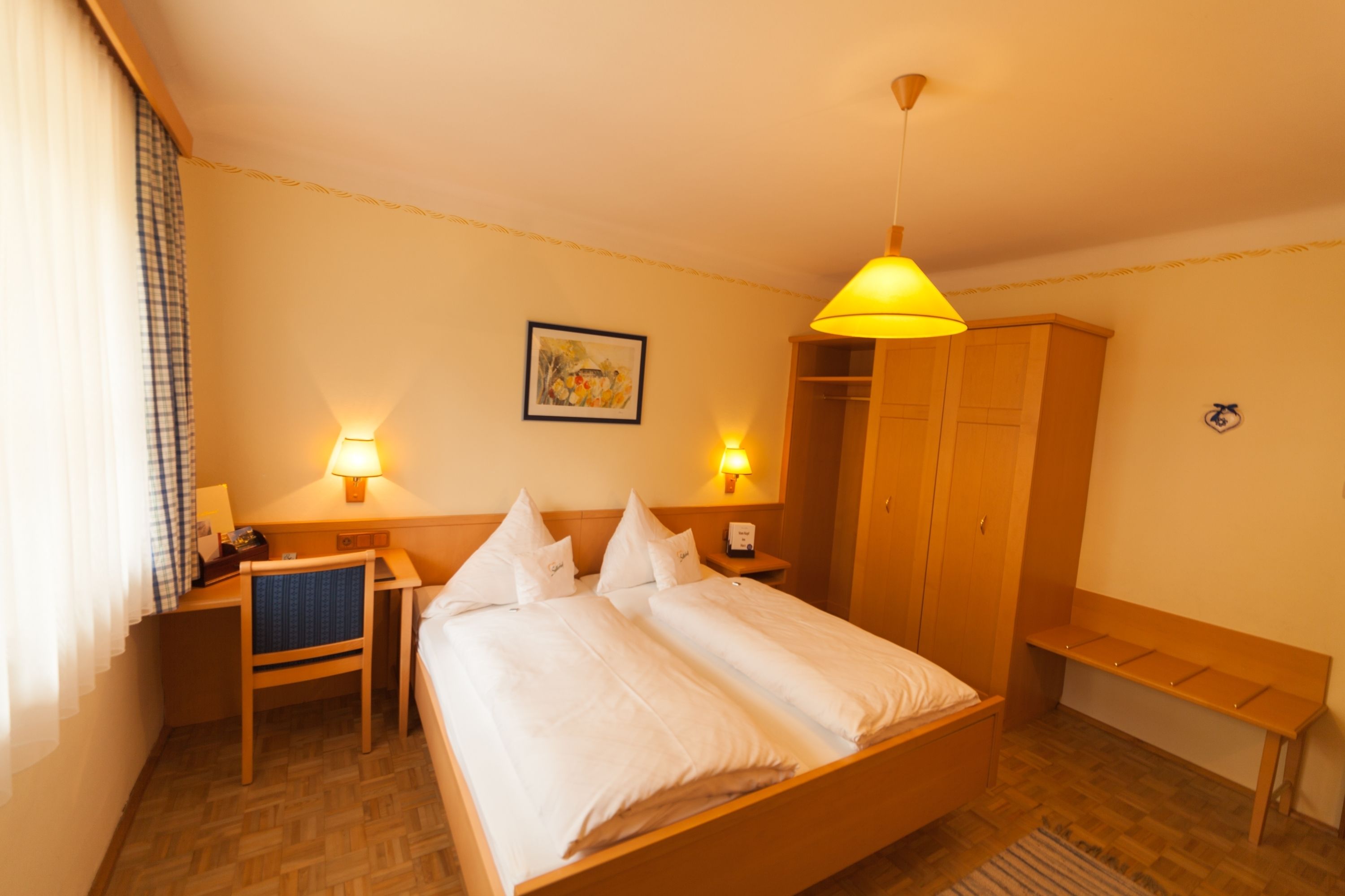 Habitación de hotel con cama, mesitas de noche, escritorio, silla, armario y banco.