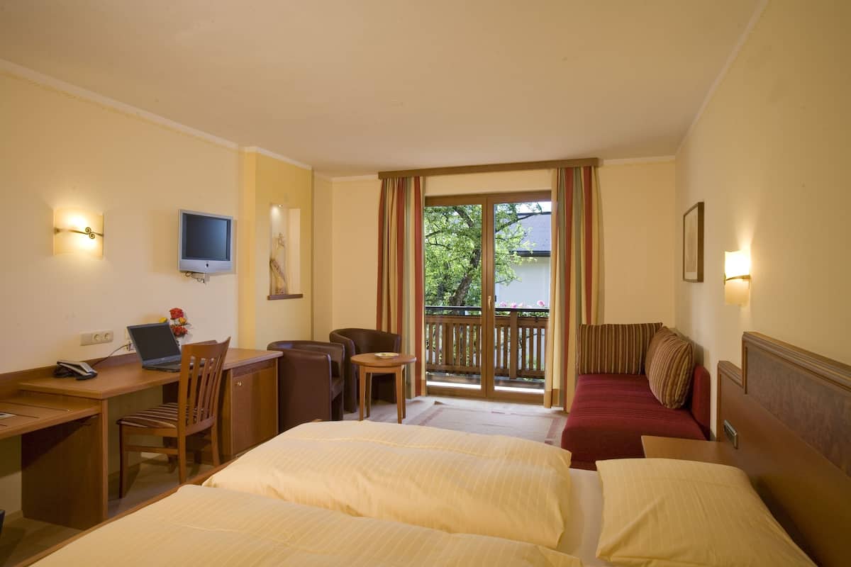 A hotel room with two beds, a desk with a laptop, a chair, a small table, and a TV mounted on the wall.