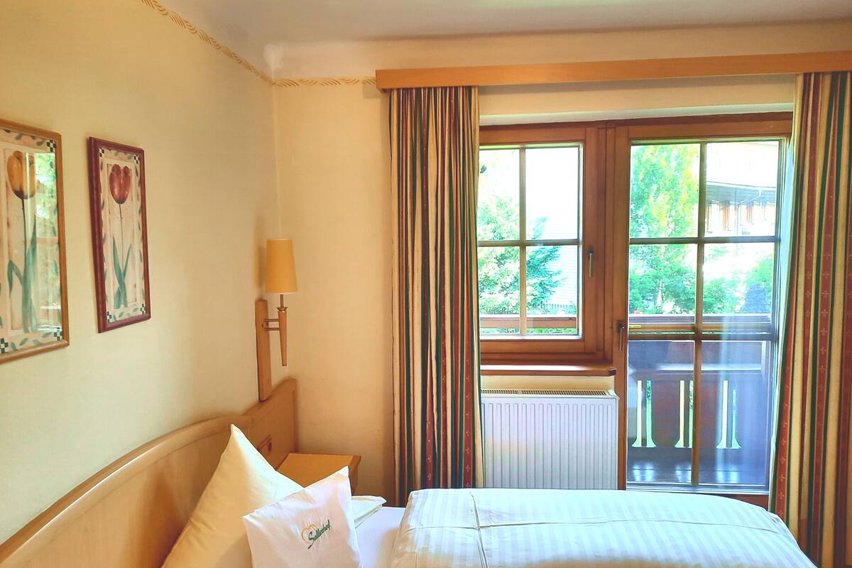 A hotel room with a bed, a nightstand, a lamp, and a window with curtains.