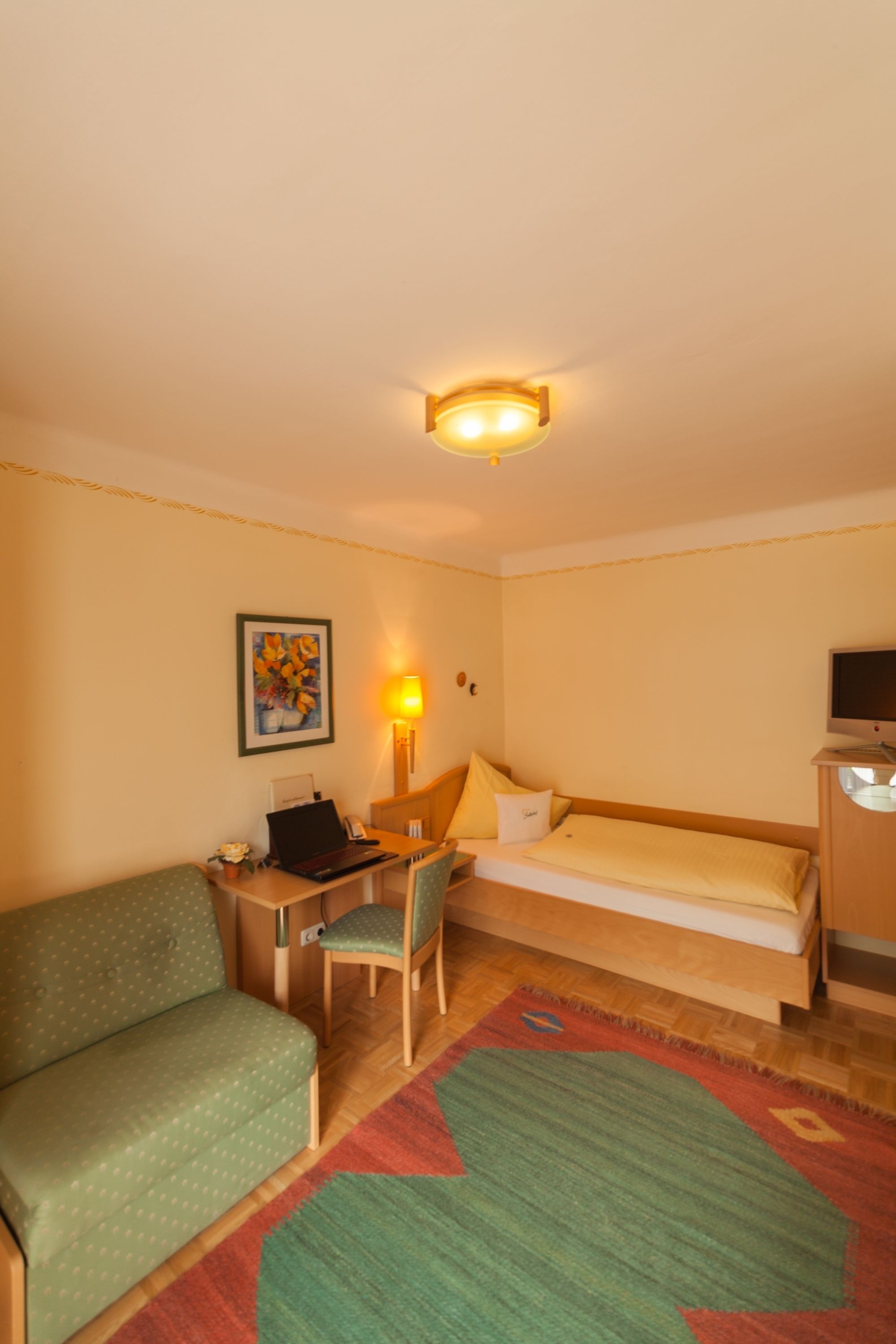 Ein Hotelzimmer mit Bett, Schreibtisch mit Stuhl, Sofa, Fernseher und einem Bild an der Wand.