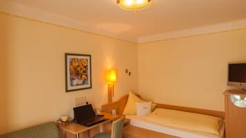 Ein Hotelzimmer mit Bett, Schreibtisch mit Stuhl, Sofa, Fernseher und einem Bild an der Wand.