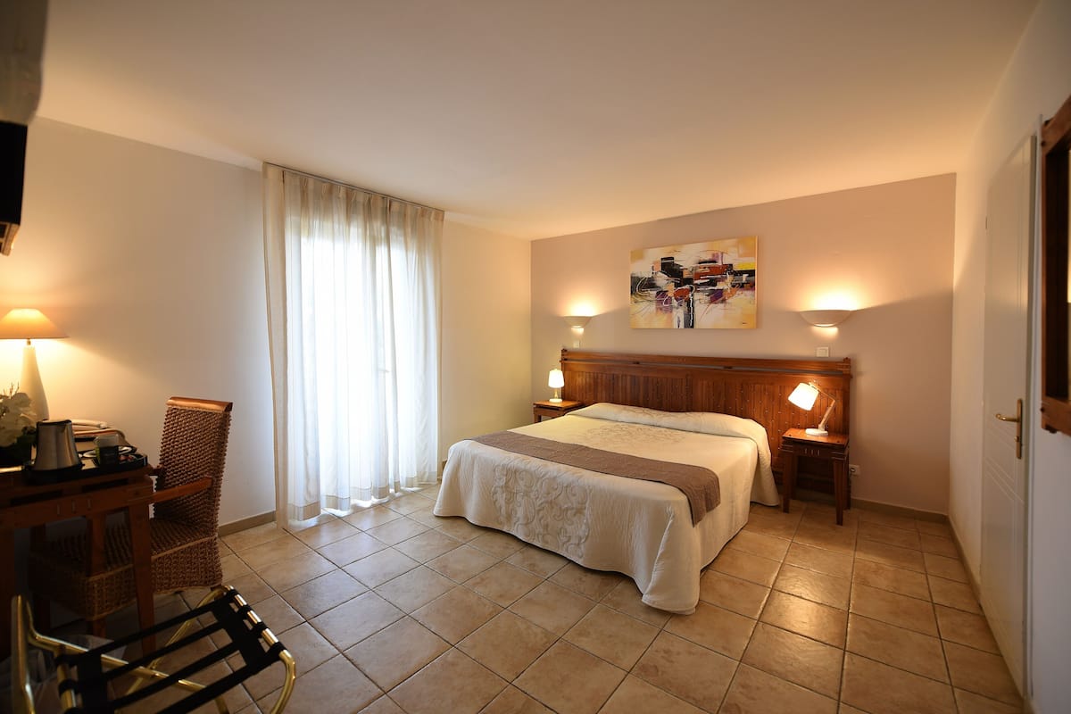 A hotel room with a bed, a chair, a table with a lamp, and a painting on the wall.