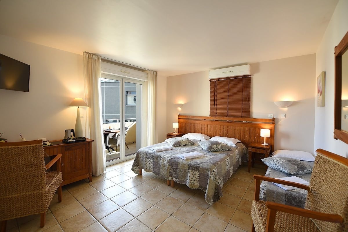A hotel room with a bed, two bedside tables, a chair, a desk, a television, and a sliding glass door to a balcony.