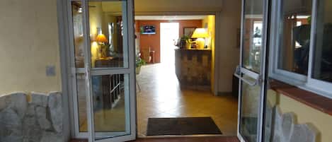 Entrada de un hotel con puerta de cristal, suelo de baldosas y pared de piedra.