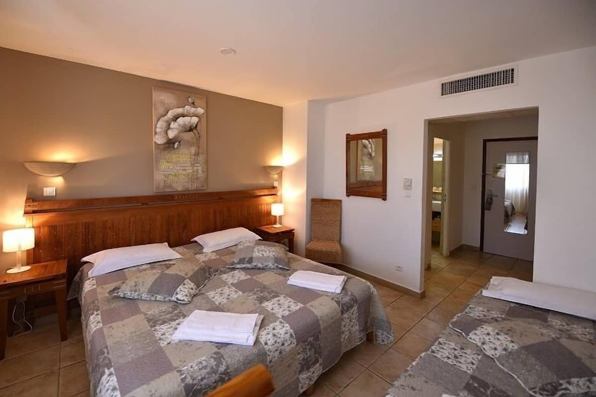 A hotel room with two beds, a wooden headboard, wall-mounted lamps, and a painting.