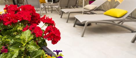 A patio area with lounge chairs and a planter with red and purple flowers.