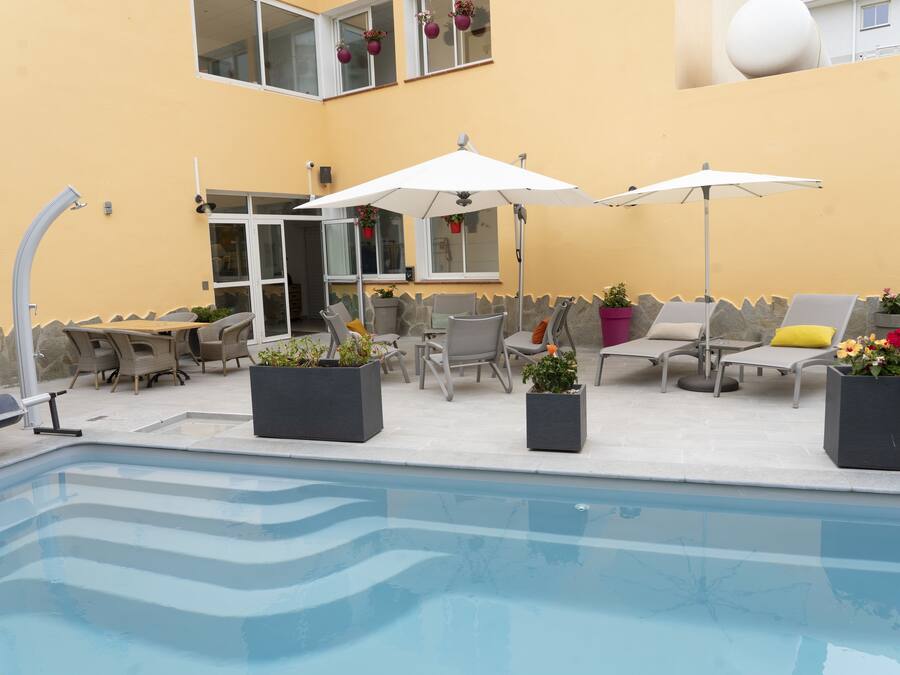 A poolside area with lounge chairs, umbrellas, and potted plants.