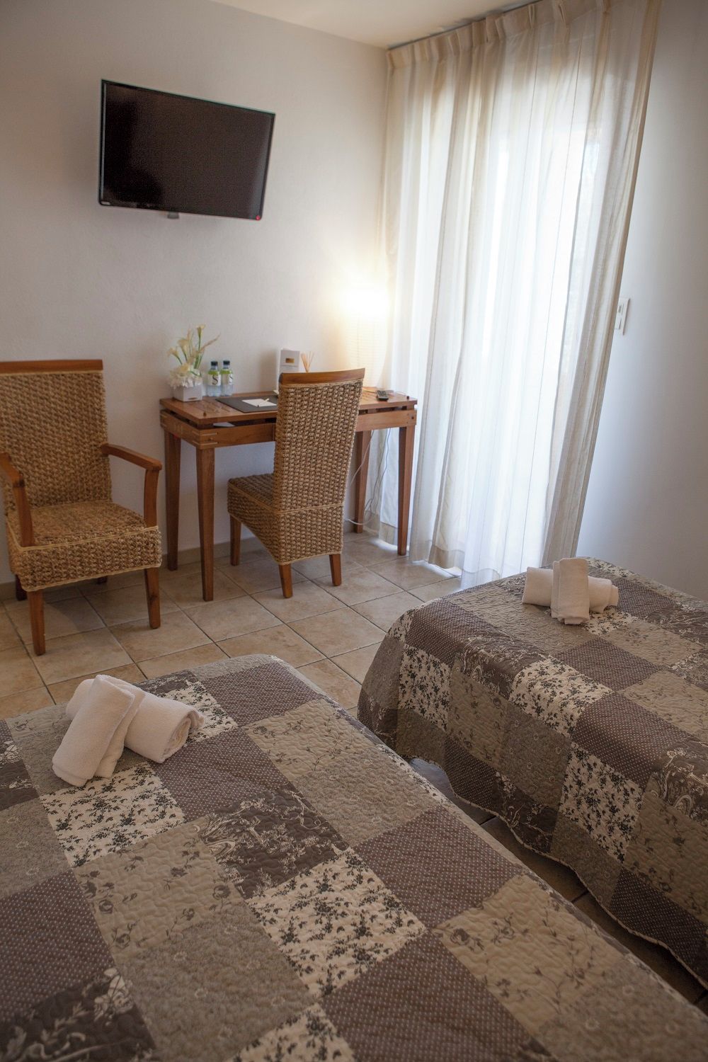 A hotel room with a bed, two chairs, a small table, a TV, and a window with curtains.