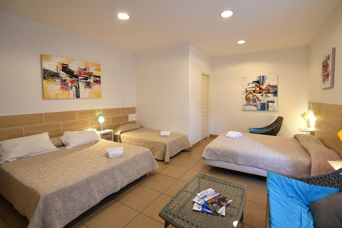 A hotel room with two beds, a small table, and artwork on the walls.