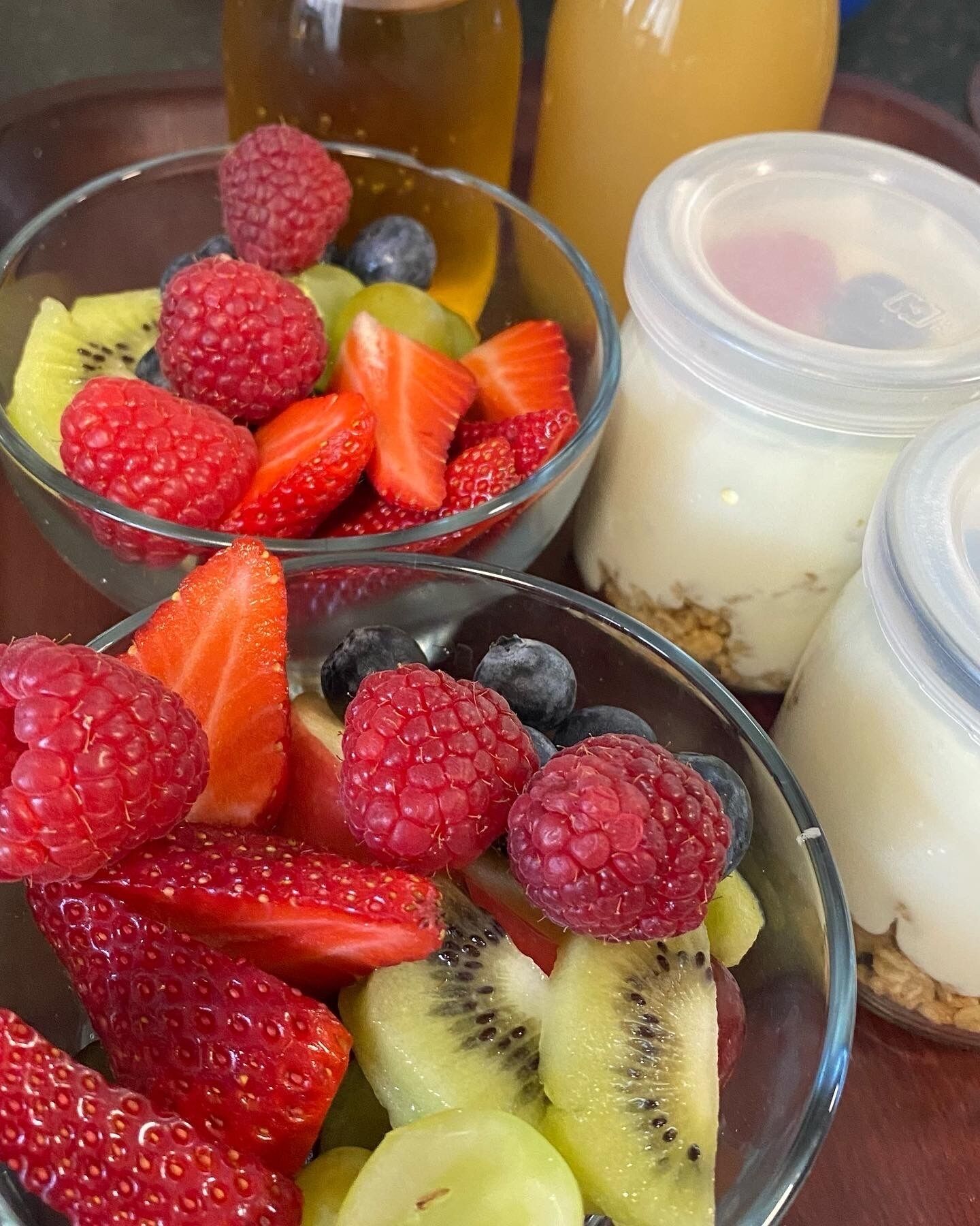 Deux bols de salade de fruits contenant des framboises, des fraises et des kiwis, et deux pots de yaourt aux fruits.