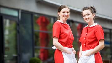 Two individuals in red and white uniforms standing in front of a building with large windows.