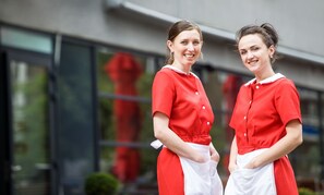 Zwei Personen in roten und weißen Uniformen stehen vor einem Gebäude mit großen Fenstern.