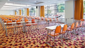 A conference room with rows of orange chairs and tables, large windows with yellow curtains, and a patterned carpet. - Iris Hotel Eden - Czech Leading Hotels (Prague)