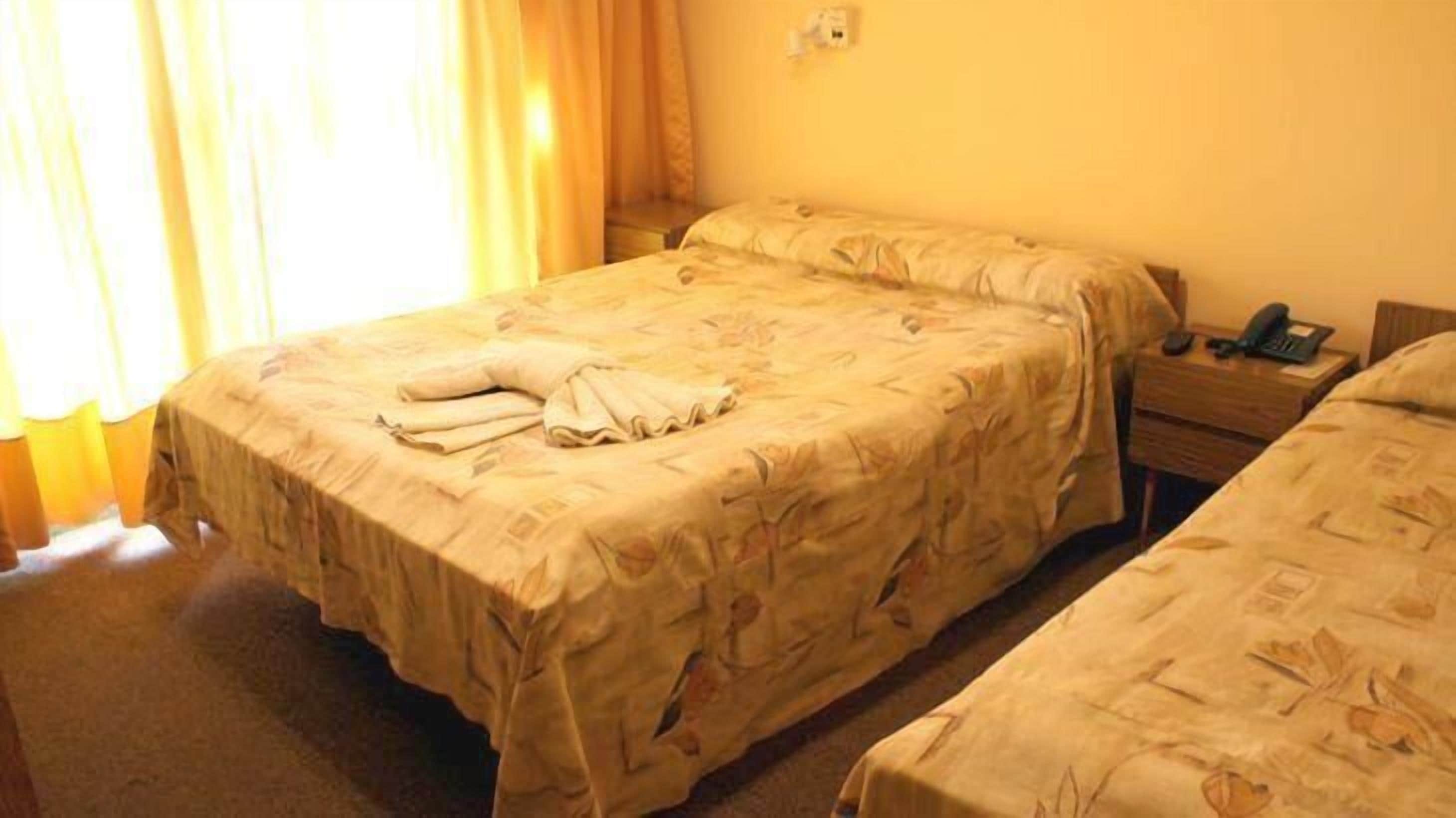 Una habitación de hotel con una cama, una mesita de noche con un teléfono y una ventana con cortinas.