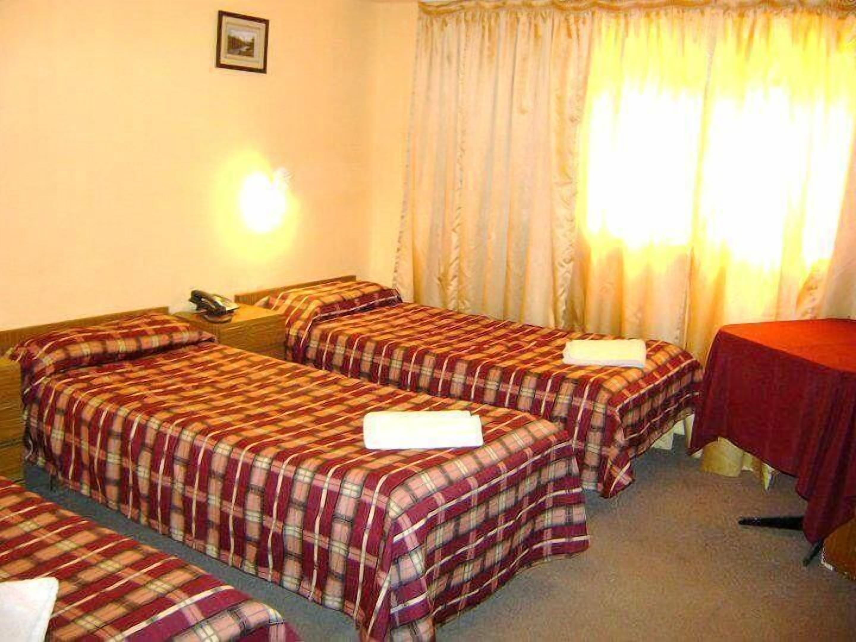 A hotel room with two beds, a small table, and a window with curtains.