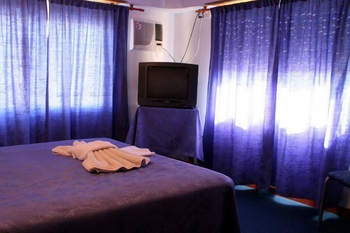 A room with a bed, a television on a stand, and curtains.