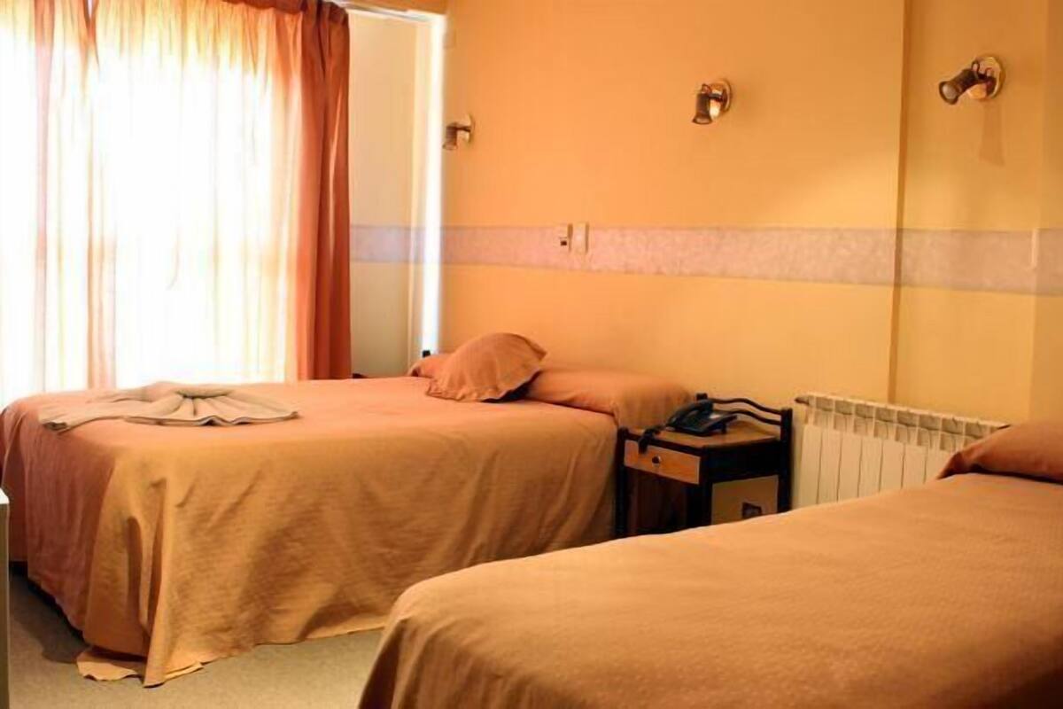 A hotel room with two single beds, a bedside table with a lamp, and a radiator.