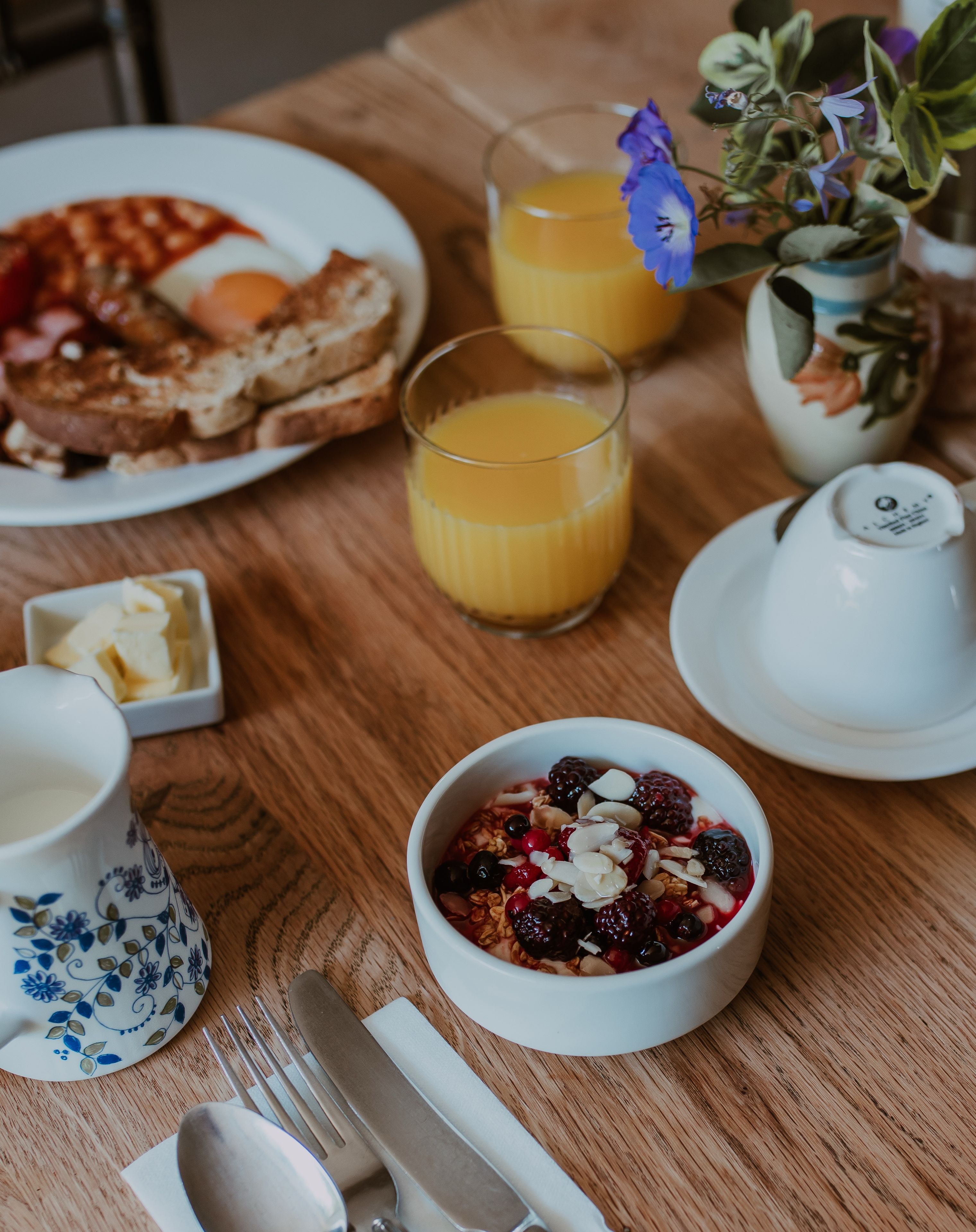 Un desayuno con tostadas, un bol de fruta, un vaso de zumo de naranja y una taza.