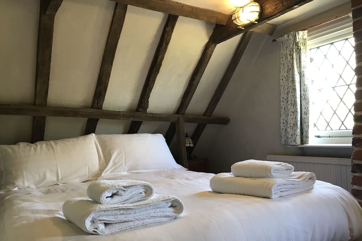 A bedroom with a large bed, wooden beams, a window with a view, and a nightstand with a lamp.