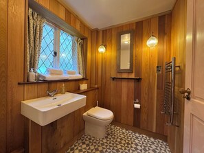 A wooden-paneled bathroom with a sink, toilet, and a window with curtains. - Strand House (Winchelsea)