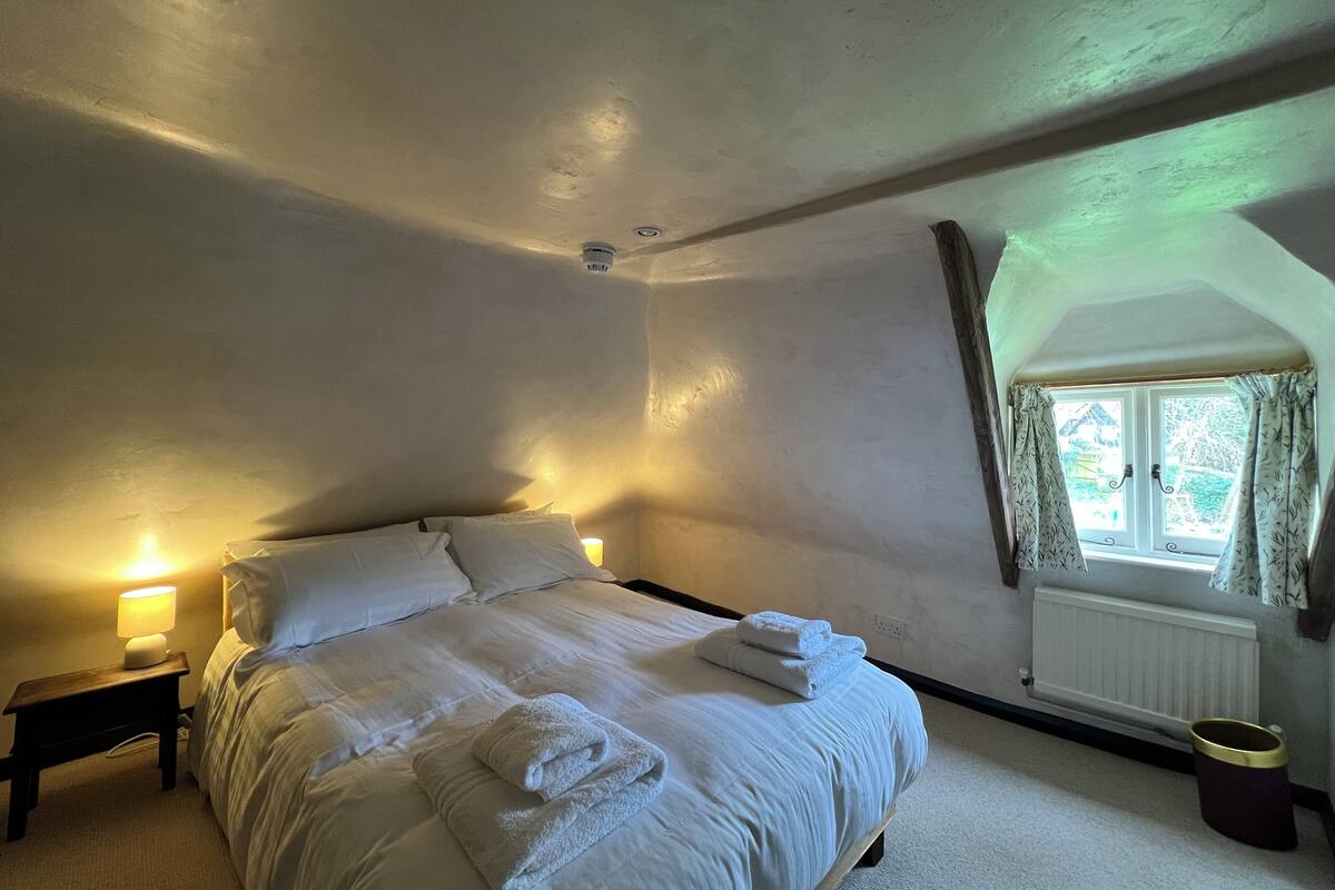 A bedroom with a large bed, bedside lamps, a window with curtains, and a radiator.