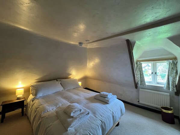 A bedroom with a large bed, bedside lamps, a window with curtains, and a radiator. - Strand House (Winchelsea)