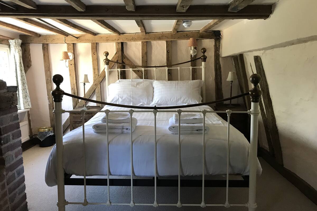 A single bed with white linens, a wooden ceiling, and a brick wall.