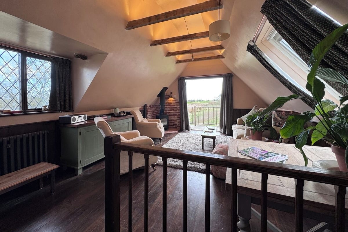 A cozy attic room with a sloped ceiling, a fireplace, a dining table, and a large window.