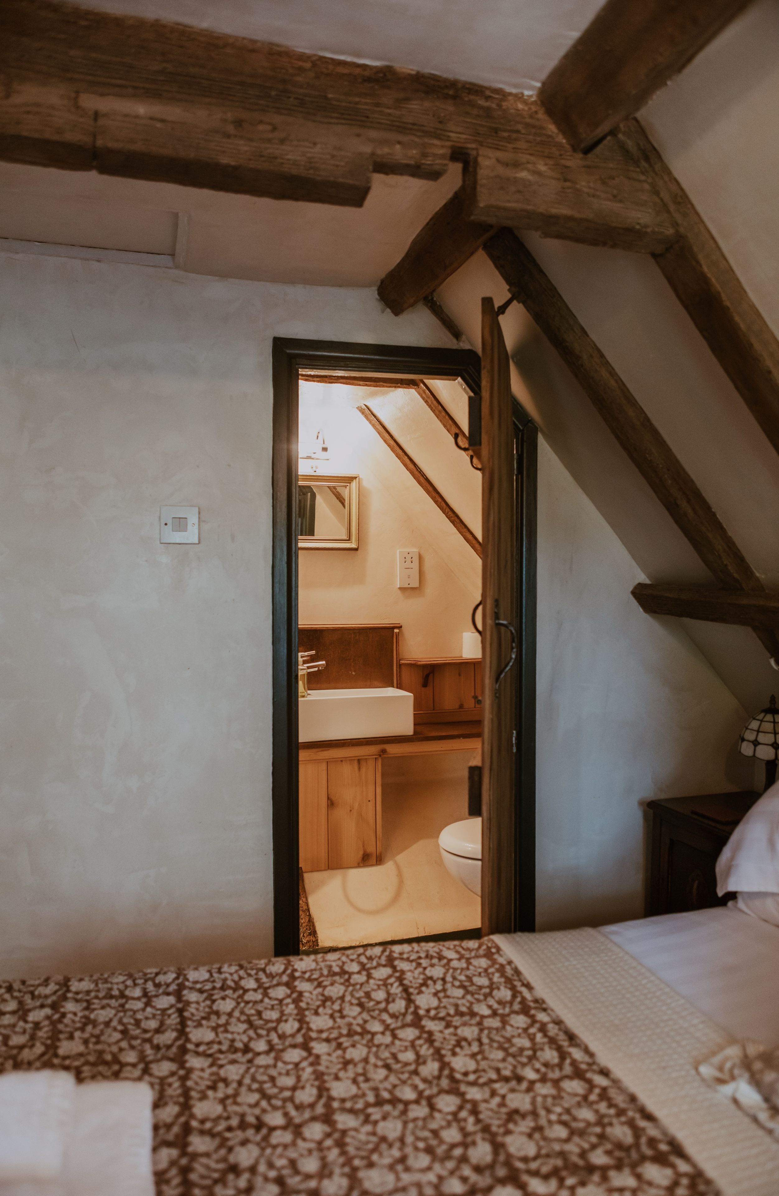 A bedroom with a bed, a wooden ceiling, a door leading to a bathroom with a sink and toilet.