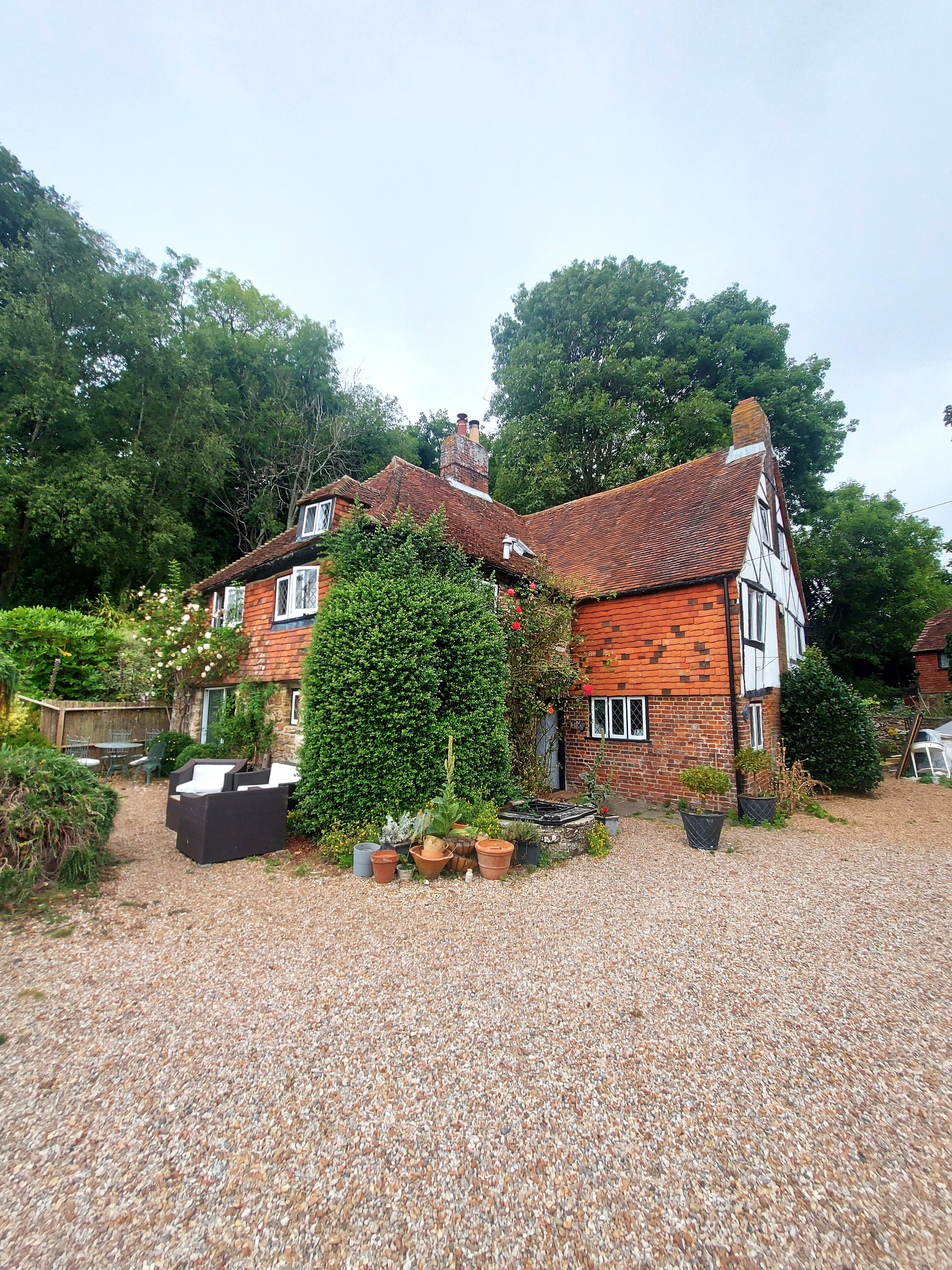 A traditional house with a gravel driveway, surrounded by lush greenery and a well-maintained garden.