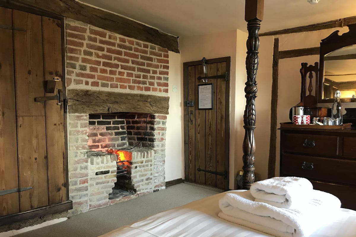 A room with a brick fireplace, wooden wardrobe, and a bed with white linens.