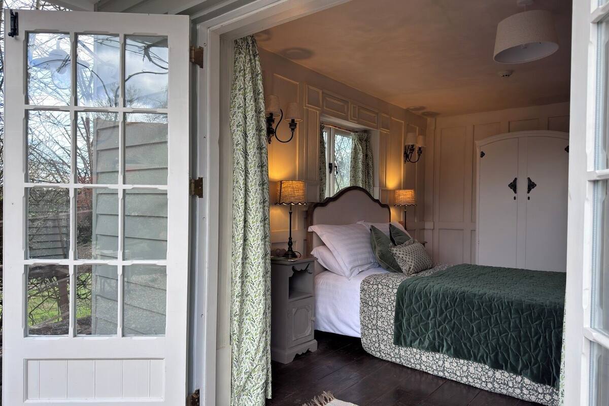 A bedroom with a bed, nightstands, lamps, a window with curtains, and a door.