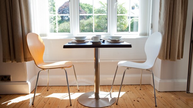 Una mesa de comedor con dos sillas, una ventana con cortinas y vistas a zonas verdes.