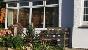 Una casa con porche cubierto, un banco de madera y un jardín con diversas plantas y flores.