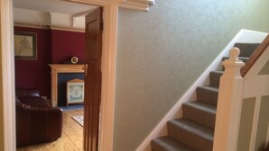 Una escalera con peldaños alfombrados y barandilla de madera, que conduce a una habitación con pared roja y chimenea.