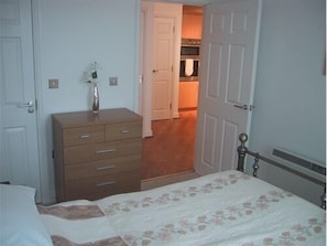 Un dormitorio con cama, cómoda y puerta que da a una cocina.