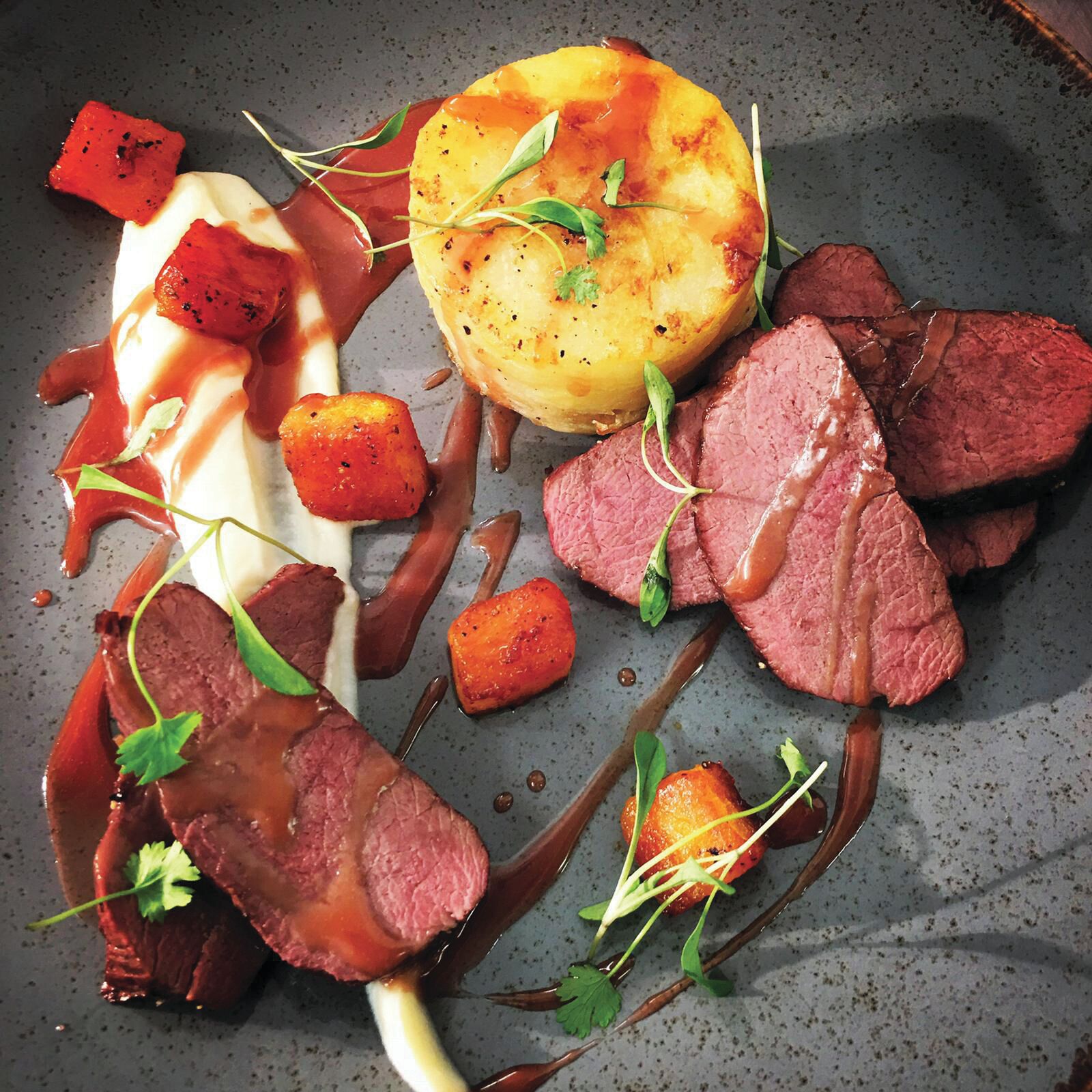A plated dish with steak, roasted potatoes, and a creamy sauce.
