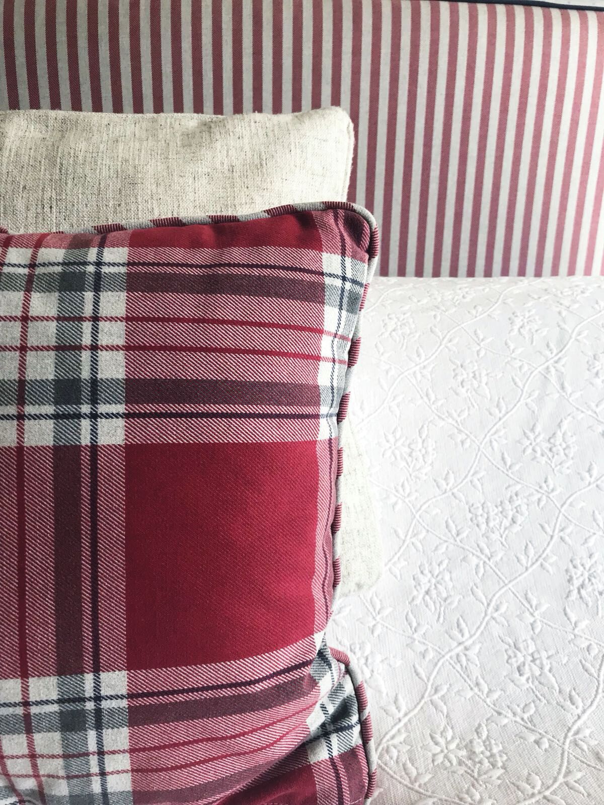 A red plaid pillow and a white pillow with a floral pattern on a striped couch.