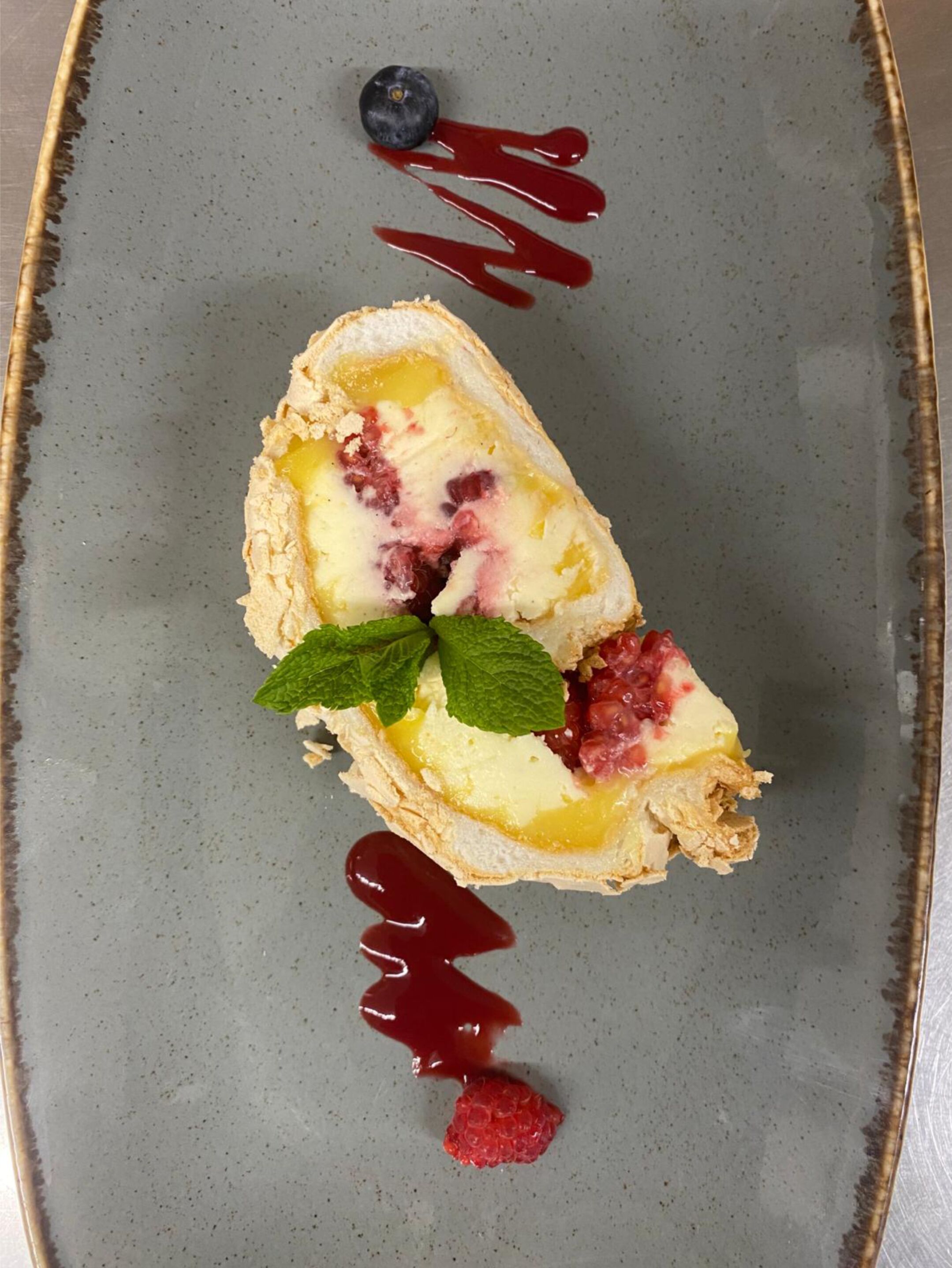A dessert on a plate with a berry compote, mint leaves, and a raspberry.
