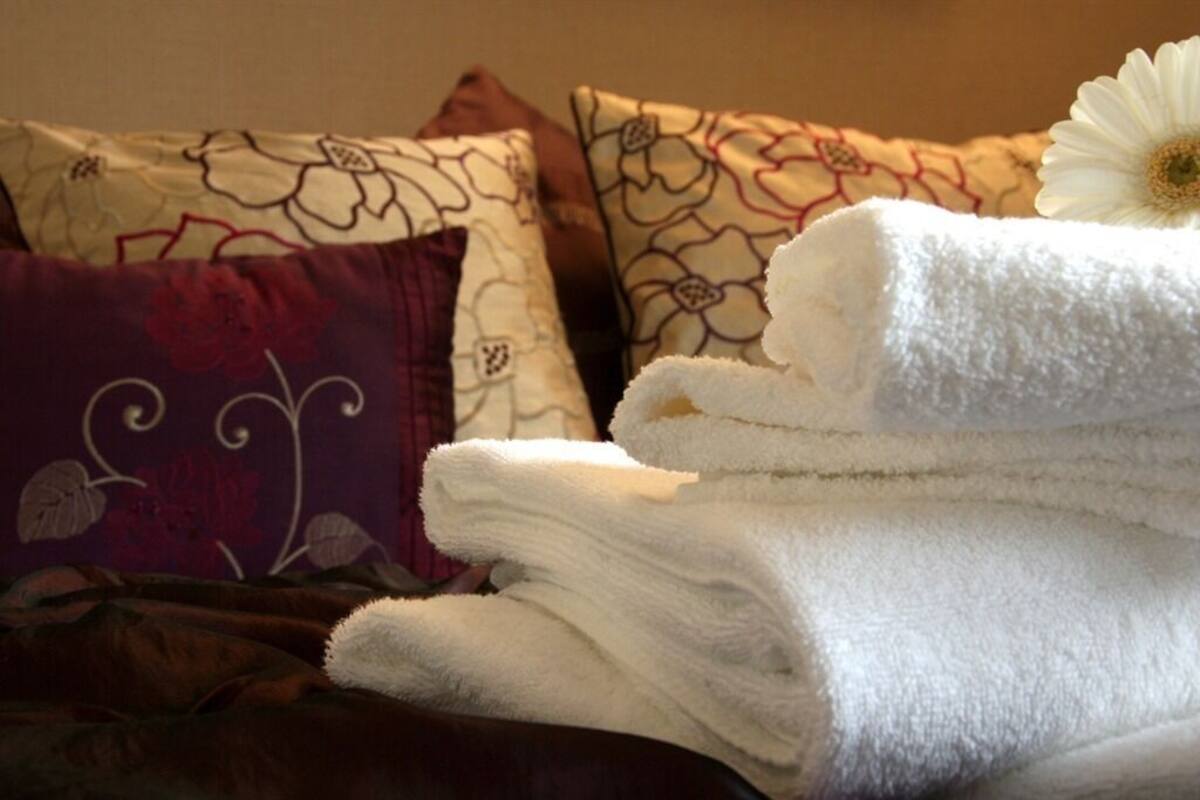 A bed with a floral-patterned pillow, a white towel, and a white flower.