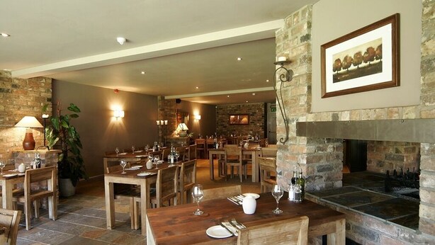 A restaurant with wooden tables and chairs, a stone fireplace, and a stone wall. - The Bell (Pershore)