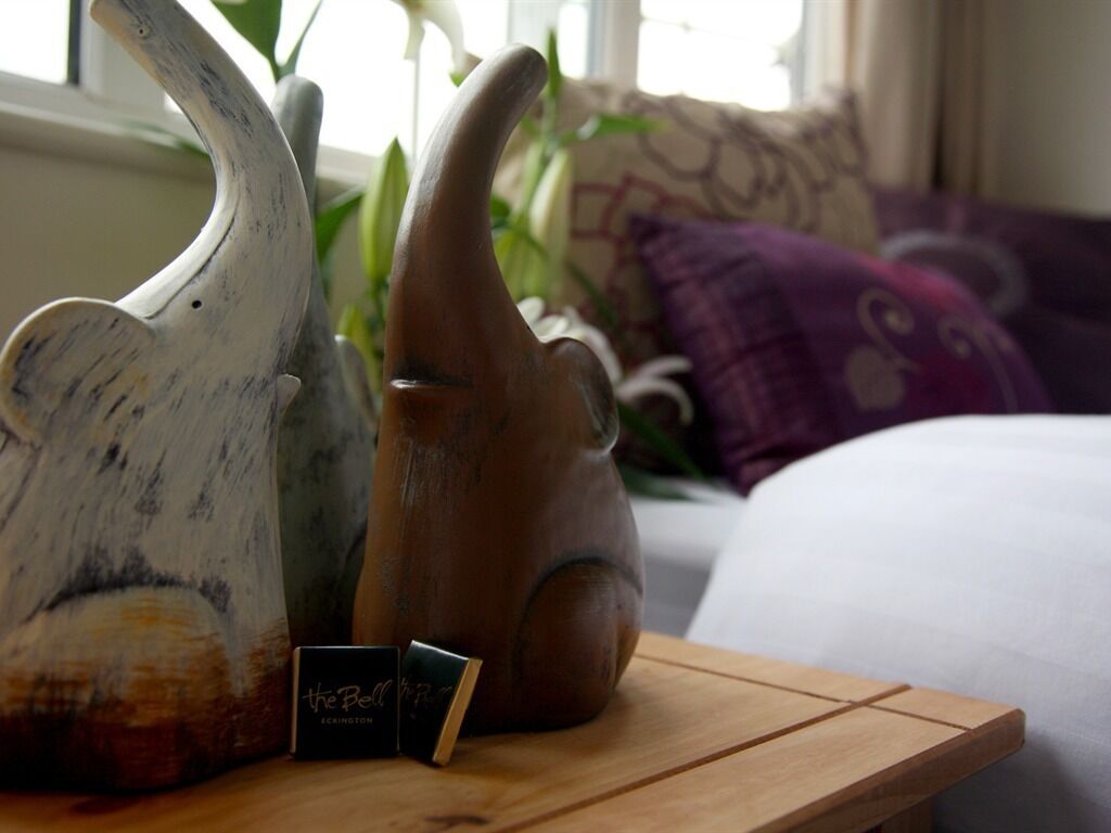A wooden table with a ceramic pig and a small card labeled "the Bell" in a room with a couch and cushions.