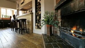A cozy interior with a fireplace, wooden flooring, and a bar area with stools. - The Bell (Pershore)