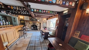 A pub with a bar area, wooden furniture, and a stone fireplace. - The Countryman's Inn (Bedale)