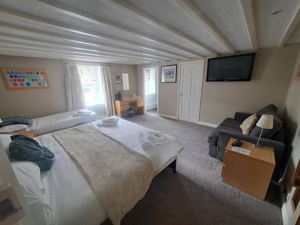 A hotel room with a large bed, a desk, a sofa, a TV, and a window with curtains. - The Countryman's Inn (Bedale)