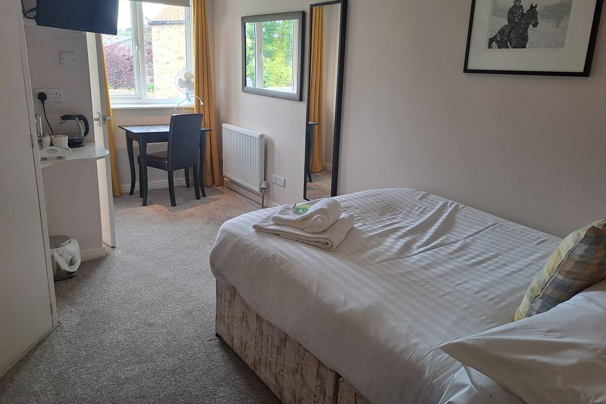 A bedroom with a bed, a desk, a chair, a radiator, and a window.